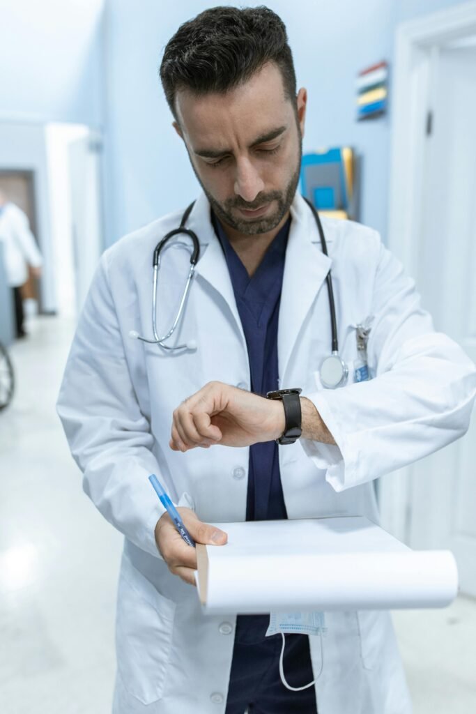 Why Do So Many Young Men Think They Have Low Testosterone? Male doctor in white coat checking watch while holding a clipboard in hospital corridor.