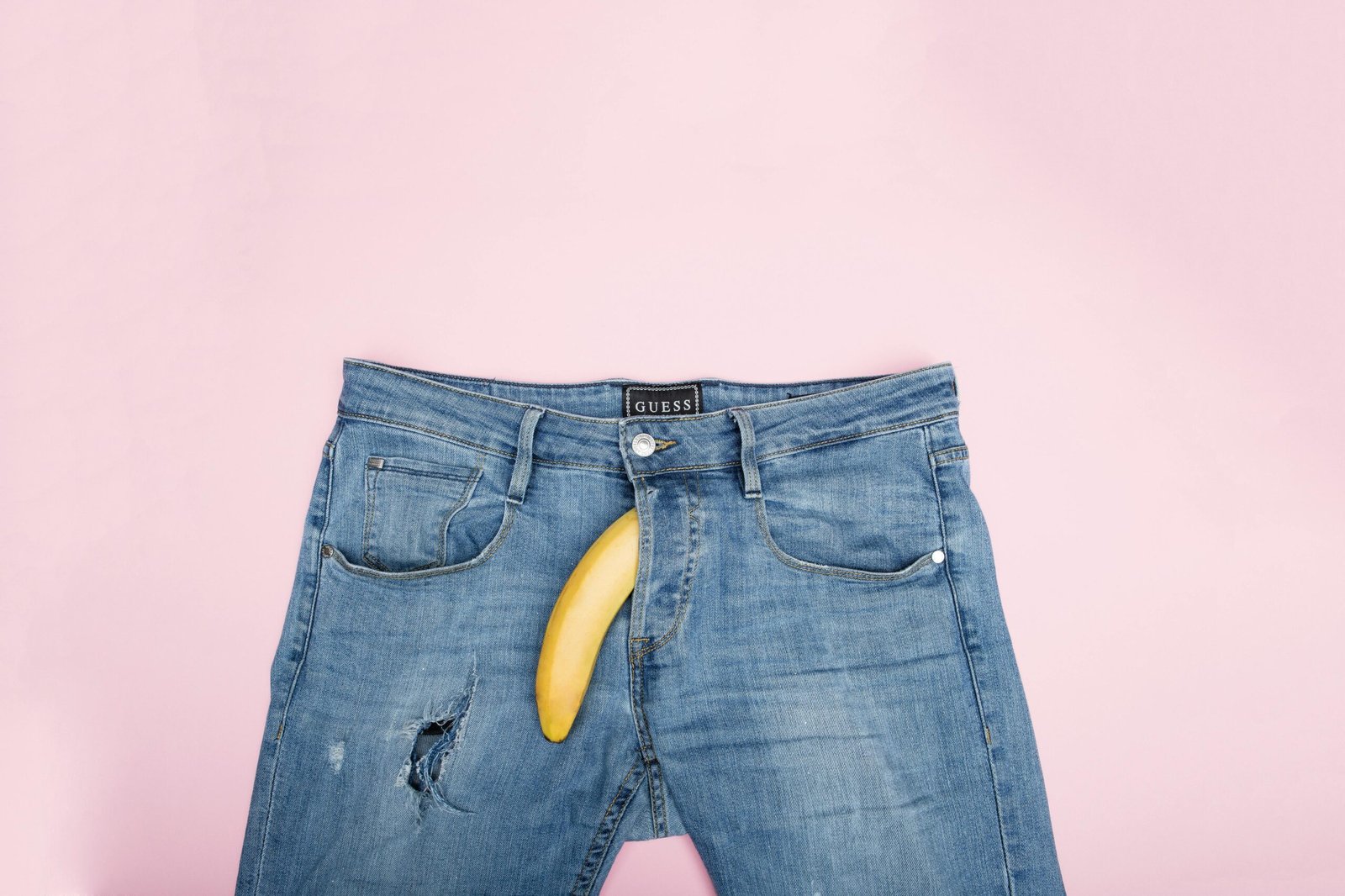 A creative still life featuring blue jeans and a banana against a pink backdrop.